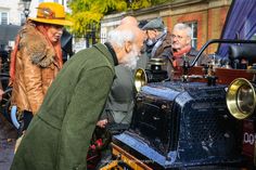 an old man is looking at an antique car on display in front of other people