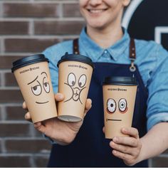 a woman holding three coffee cups with faces drawn on them