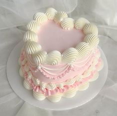 a heart shaped cake on a plate with white and pink icing around the edges