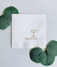 a napkin with a happy birthday written on it next to some green leafy leaves