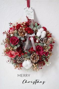 a christmas wreath hanging on the wall with pine cones and red flowers in front of it