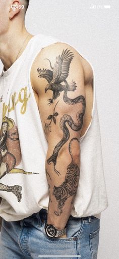 a man with a dragon tattoo on his arm and shoulder, standing in front of a white wall