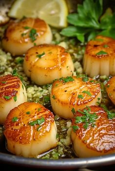 some scallops are cooking in a pan with lemon wedges and parsley