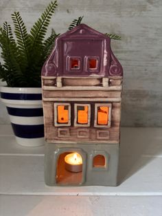 a small ceramic house with a lit candle in the front and potted plant behind it