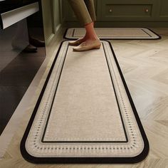 a person standing on a rug in the middle of a kitchen with green cabinets and wooden floors