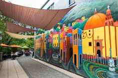 a mural on the side of a building with people sitting at tables under umbrellas