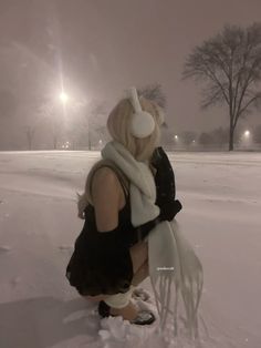 a woman kneeling down in the snow with her headphones on and scarf around her neck