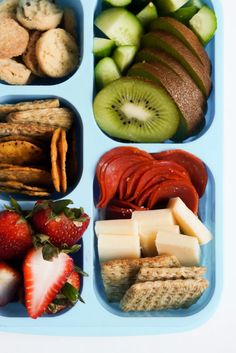 a blue tray filled with different types of food on top of a white table next to strawberries and cucumbers