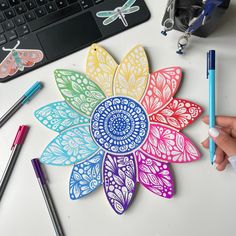 a person is drawing with colored paper on a table next to a keyboard and pencils