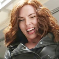 a woman with red hair laughing and wearing a leather jacket