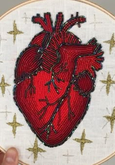 a hand is holding up a small embroidered heart on a white background with gold stars