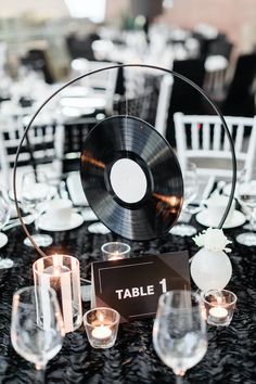 the table is set up with candles and music disc centerpieces for an elegant black and white wedding