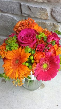 a vase filled with orange and pink flowers on top of a stone wall next to a brick wall