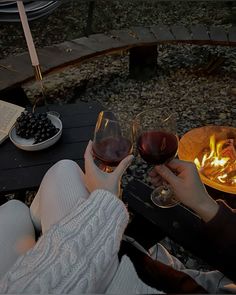 two people toasting glasses of wine in front of an open fire pit