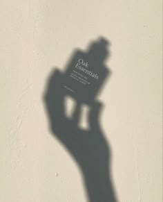 the shadow of a person's hand holding an object in front of a white wall