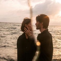 a man and woman standing next to each other near the ocean with their hands on their face