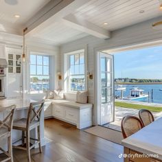 an open kitchen and dining area with white walls, wood floors and windows overlooking the water