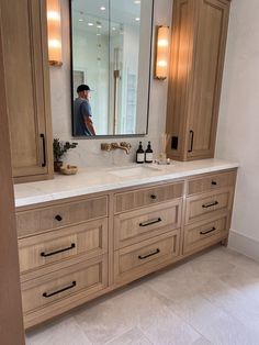 a man is standing in front of a large bathroom mirror and vanity with two sinks