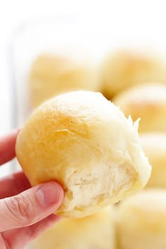 a hand holding a piece of bread in front of some other rolls on a plate