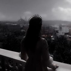 a woman standing on top of a balcony looking out at the water and buildings in the distance