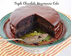 a chocolate cake on a glass plate with a spoon in it and text overlay that reads triple chocolate mayonnaise cake