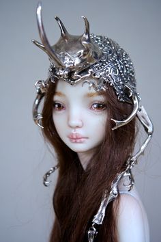 a close up of a doll wearing a metal head piece with horns and chains on it