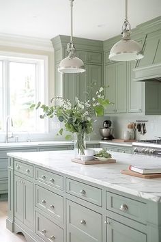 a kitchen with green cabinets and marble counter tops, two pendant lights over the island