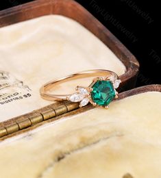 an emerald and diamond ring sitting in a wooden box on top of a piece of paper