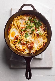 a skillet filled with pasta and eggs on top of a white tablecloth next to a napkin