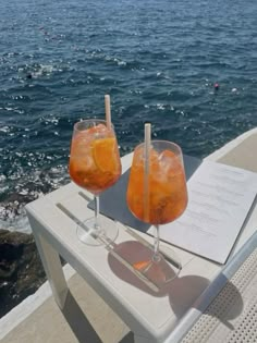 two drinks are sitting on a table near the water