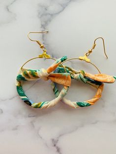 two pieces of fabric wrapped around each other on top of a marble table with gold ear wires