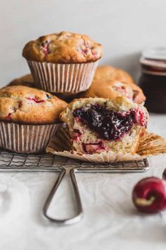 several muffins on a cooling rack with cherries in the foreground and an apple in the background