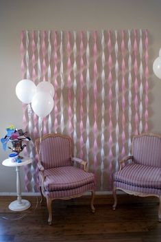 two chairs sitting next to each other in front of a wall with balloons on it