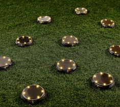 there are many round metal plates on the grass with lights around them, all in different shapes and sizes