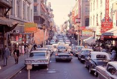 an old photo of cars and people on the street in front of buildings with neon signs