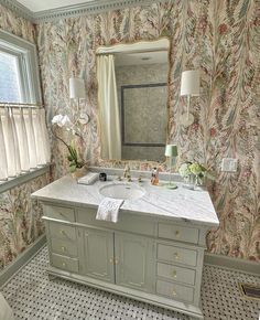 a bathroom with floral wallpaper and marble counter tops, along with a large mirror