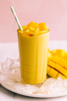 a glass filled with mango juice next to sliced mangoes on a plate and ice