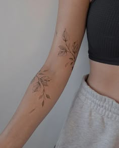 a woman's arm with leaves on it and a tattoo design on the wrist