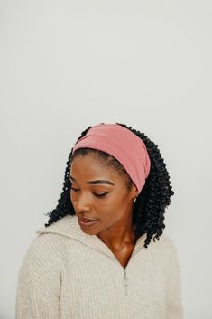 a woman wearing a pink headband looking down at her cell phone while standing in front of a white wall