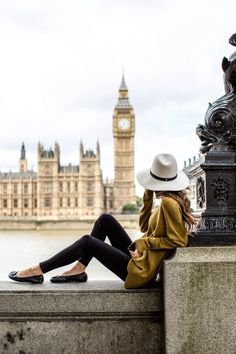 a woman sitting on the edge of a wall next to a clock tower