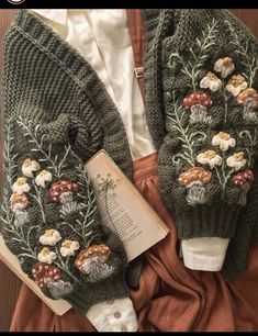 an open book laying on top of a bed next to two knitted mittens