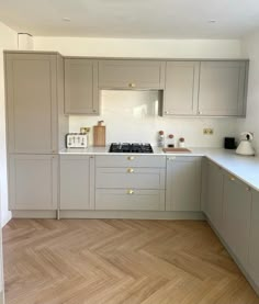 an empty kitchen with wooden floors and gray cabinets on the wall, along with white counter tops