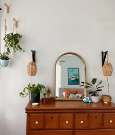 there is a dresser with plants on it and a mirror in the corner next to it