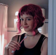 a woman with pink hair is holding a toothbrush in her hand and smiling at the camera