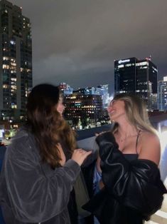 two women standing next to each other in front of a cityscape at night