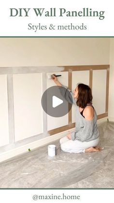 a woman is painting the walls in her living room with white paint and she is sitting on the floor