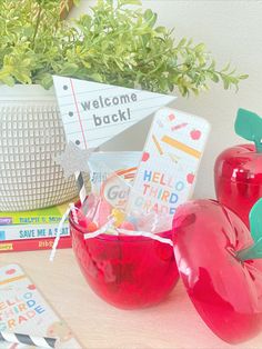 there are two red apples in the bowl on the table next to books and a potted plant