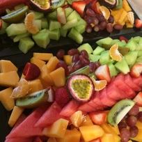 several different types of fruit are arranged on black trays, including grapes, melon, kiwi, and pineapple