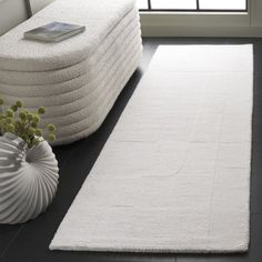 a large white rug on the floor in front of a window with a vase and plant