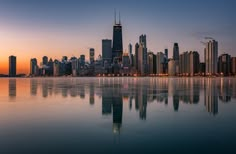 the city skyline is reflected in the water at sunset or dawn, as seen from across the bay